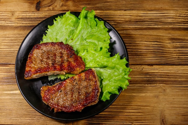 Grilled pork steaks with lettuce leaves on wooden table Top view