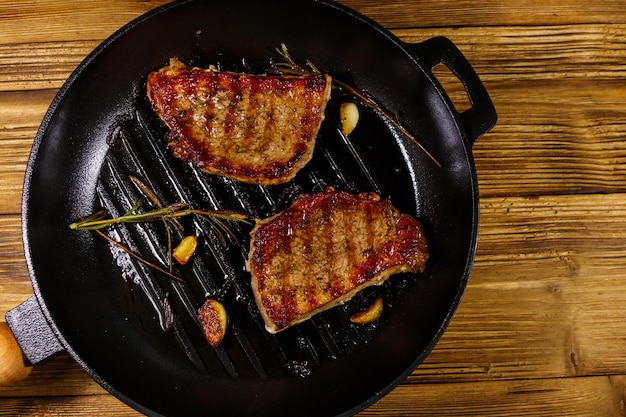 Grilled pork steaks with rosemary garlic and spices in cast iron grill frying pan on wooden table Top view