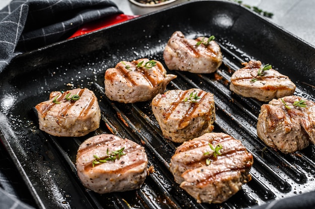 Grilled pork tenderloin medallions with fresh herbs in a pan. gray background. Top view