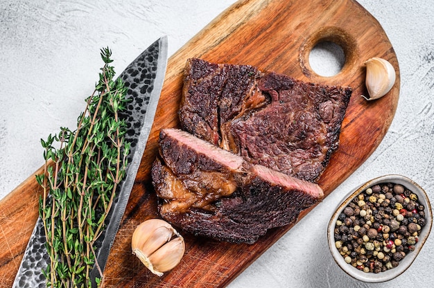 Grilled prime rib eye beef meat steak on a wooden cutting board on white. Top view.