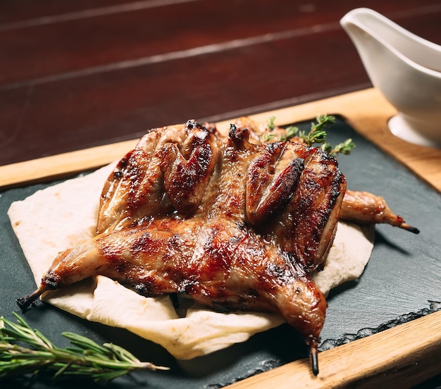 Grilled quails on wooden plate.