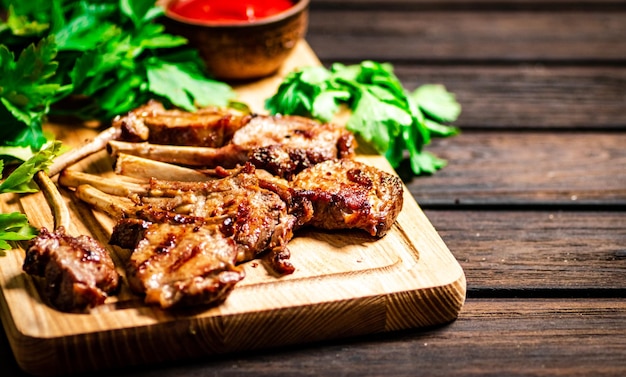 Grilled rack lamb on a cutting board with tomato sauce and parsley