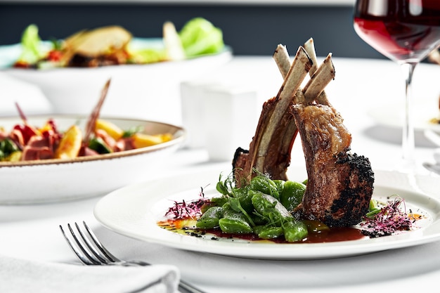 Grilled rack of lamb on a white plate with stewed bean pods. Grilled lamb with a glass of wine on a light background.