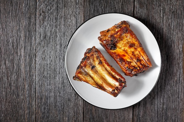 Grilled rack of spare pork ribs on a plate on a dark wooden table horizontal view from above