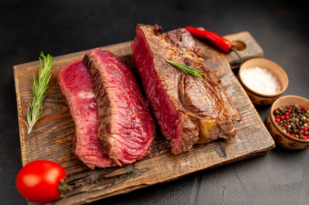 Grilled rib eye beef steak with herbs and spices on a stone background