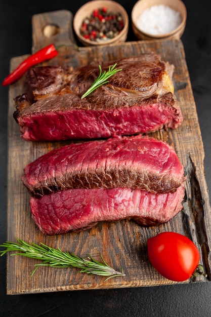 Grilled rib eye beef steak with herbs and spices on a stone background