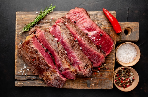 Grilled rib eye beef steak with herbs and spices on a stone background