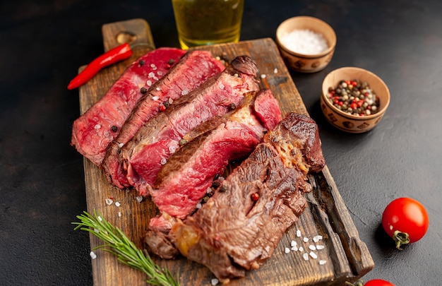 Grilled rib eye beef steak with herbs and spices on a stone background