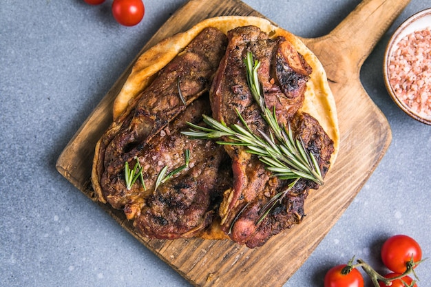 Grilled rib eye steak ribeye beef marbled meat on a board with tomato Black background top view Copy space