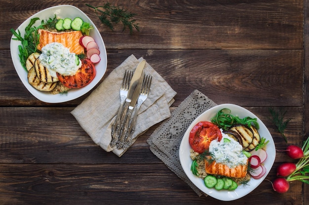 Grilled salmon eggplants and tomatoes with quinoa and tzatziki sauce on rustic wooden background Healthy dinner Top view