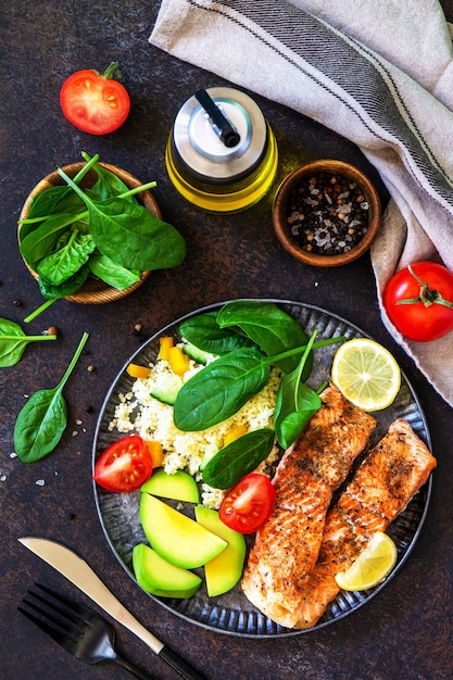 Grilled salmon fillet with couscous salad fresh vegetables and avocado on dark background Top view flat lay