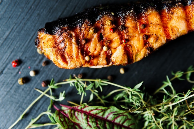 Grilled salmon fish fillet with green salad on the black cutting board close up