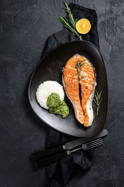 Grilled salmon steak garnished with rice and spinach. Black background. Top view. Space for text