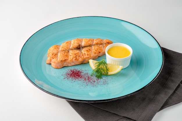 Grilled salmon steak with lemon and sauce on colorful plate and napkin on white background