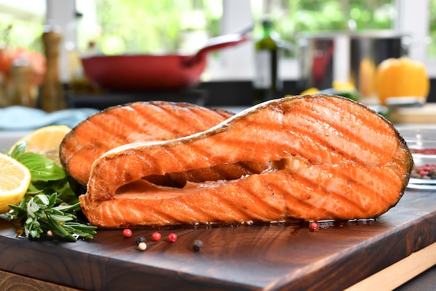 Grilled salmon steaks with ingredients on wooden cutting board in the kitchen