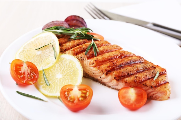 Grilled salmon and vegetables on plate on wooden background