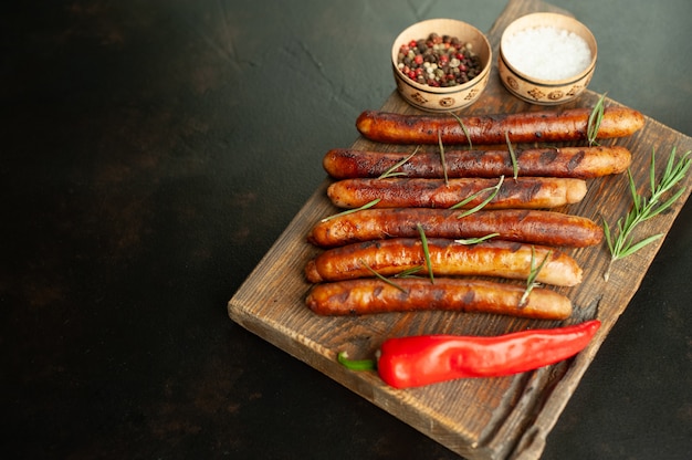 grilled sausages on a cutting board with spices and rosemary on a stone table with copy space for your text