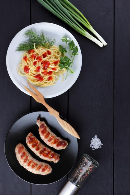 Grilled sausages on dark background Spaghetti with sauce and greens on white plate Pasta and meat dish on grill Top view