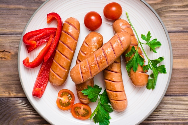 Grilled sausages near tomatoes and peppers on a plate