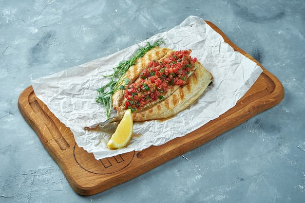 Grilled sea bass fish with tomato salsa on a wooden board. Cooked seafood