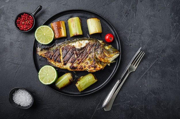 Grilled sea bream or dorado raw fish on black plate with Braised Leeks over textured black background