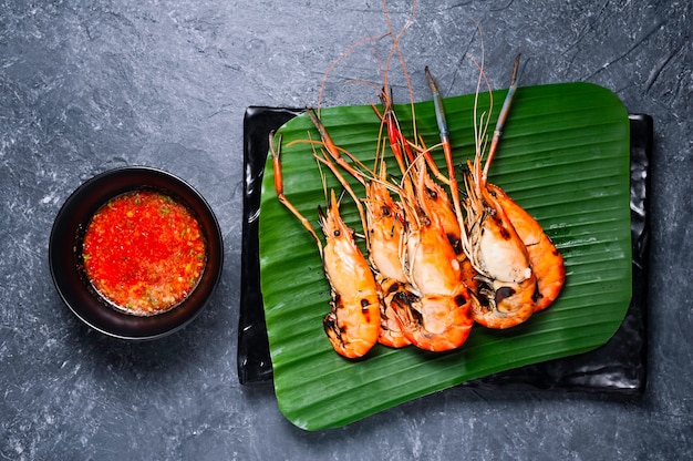 Grilled shrimp on black plate with spicy sauce on table.