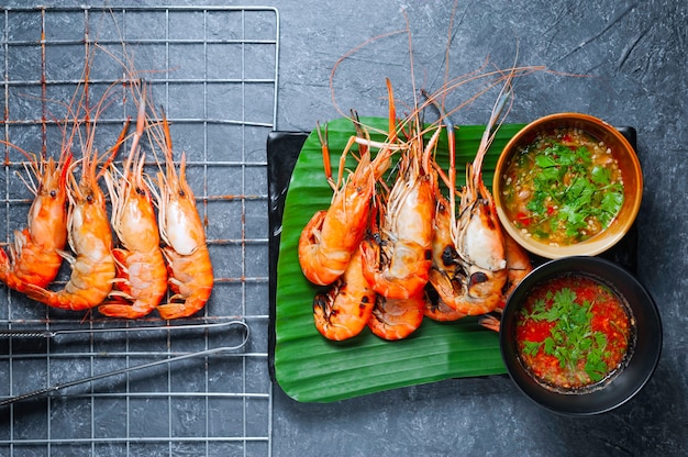 Grilled shrimp on black plate with spicy sauce on table.