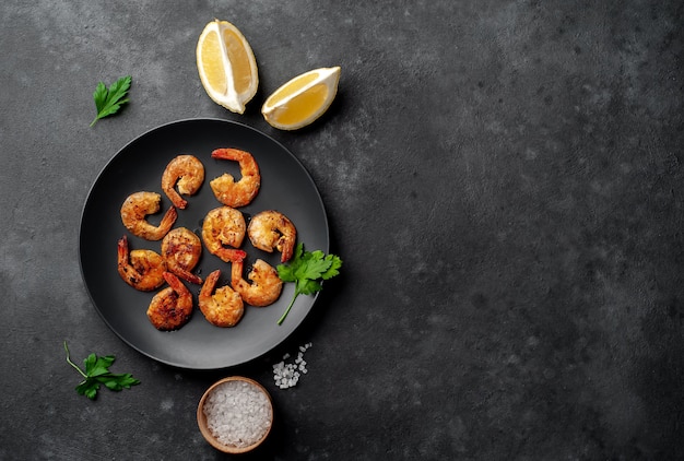 grilled shrimps, with lemons, herbs and spices, served on a black plate on a stone background