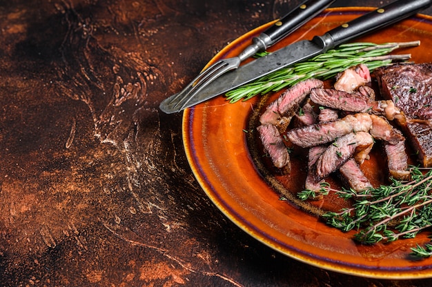 Grilled sliced rib eye or ribeye beef meat steak on a rustic plate on black. Top view.