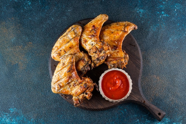 Grilled spicy chicken wings with ketchup on a black plate on a dark slate stone or concrete background Top view with copy space BBQ concept