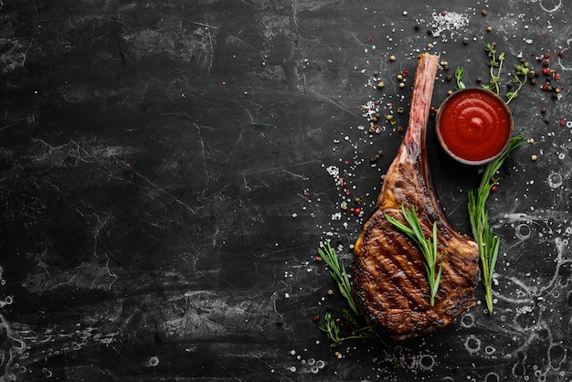 Grilled steak on the bone Tomahawk steak on a black stone background Top view Free copy space