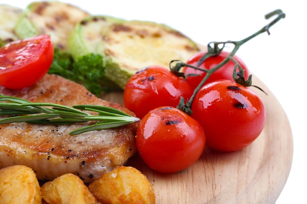 Grilled steak with fried potato pieces and grilled vegetables on wooden board isolated on white