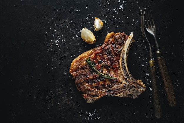 Grilled steak with spices on dark with cutlery.