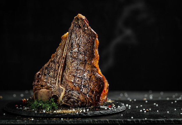 Grilled T-bone steak on stone table. juicy steak rare beef with spices on a black table, banner, menu, recipe, place for text..