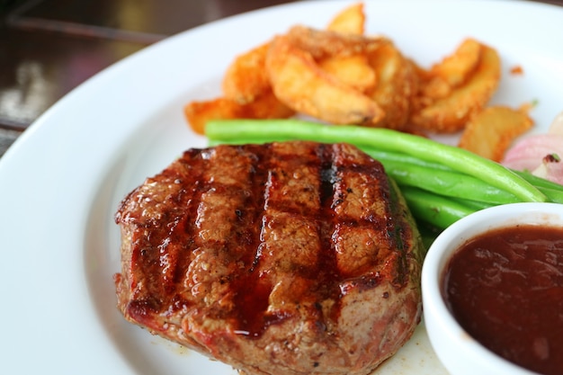 Grilled Tenderloin Steak with Blurred Steamed Vegetables and Fried Potatoes in Background