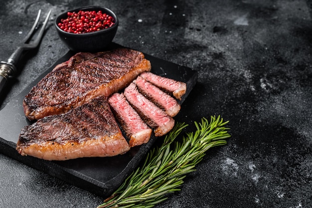 Grilled top sirloin or cup rump beef meat steak on marble board Black background Top view Copy space