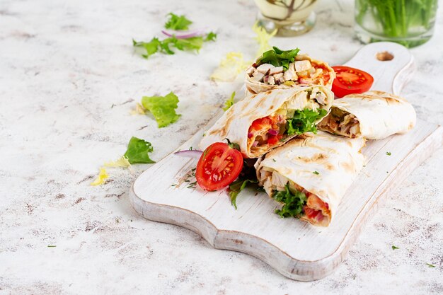 Grilled tortilla wraps with chicken and fresh vegetables on white wooden board Chicken burrito Mexican food Healthy food concept