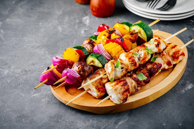 Grilled vegetable and chicken skewers with sweet corn paprika zucchini onion tomato and mushroom on a wooden plate