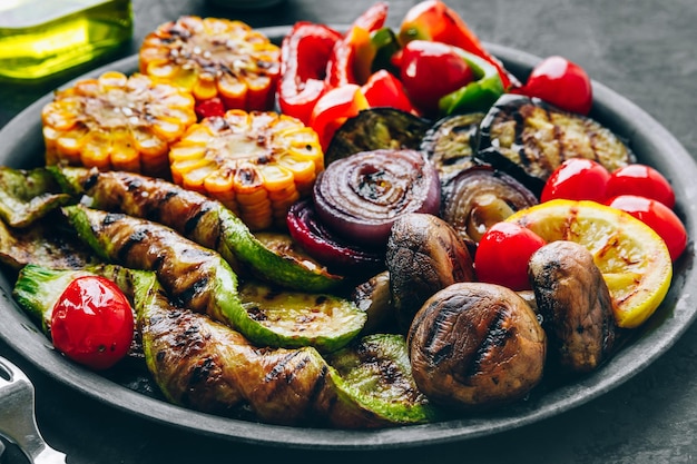 Grilled vegetables in bowl on dark stone background Zucchini bell peppers sweet corn tomatoes red onions and eggplant