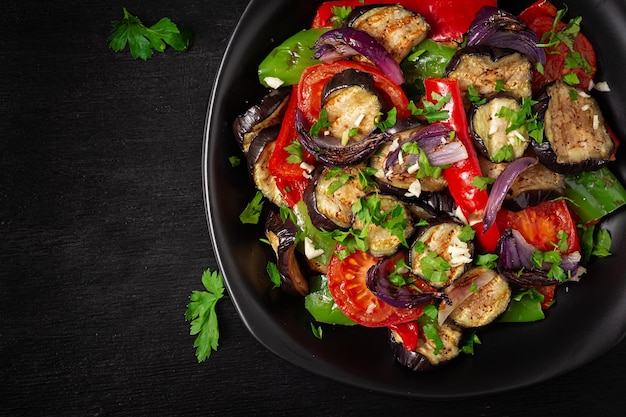 Grilled vegetables eggplant bell pepper zucchini red onion tomato with garlic on a black plate Top view above