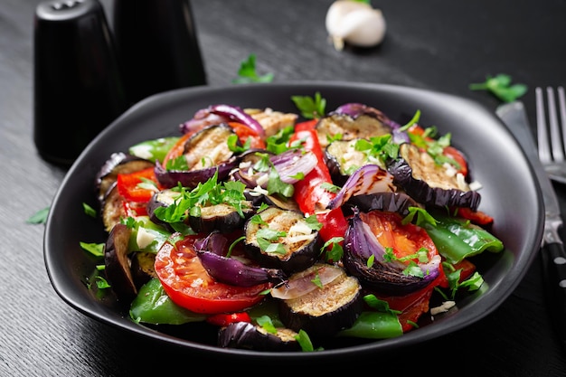 Grilled vegetables eggplant bell pepper zucchini red onion tomato with garlic on a black plate