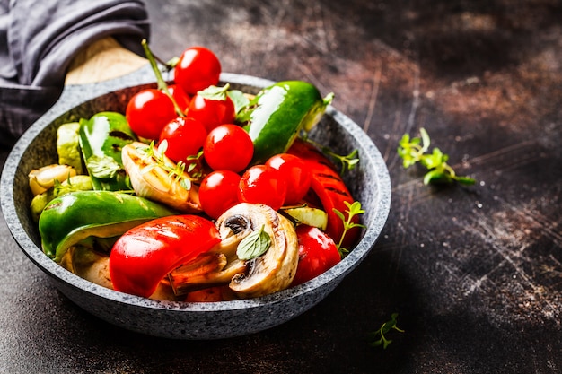 Grilled vegetables (peppers, zucchini, mushrooms and tomatoes in pan, dark background. 