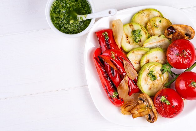 Grilled vegetables on a plate with pesto on white wood