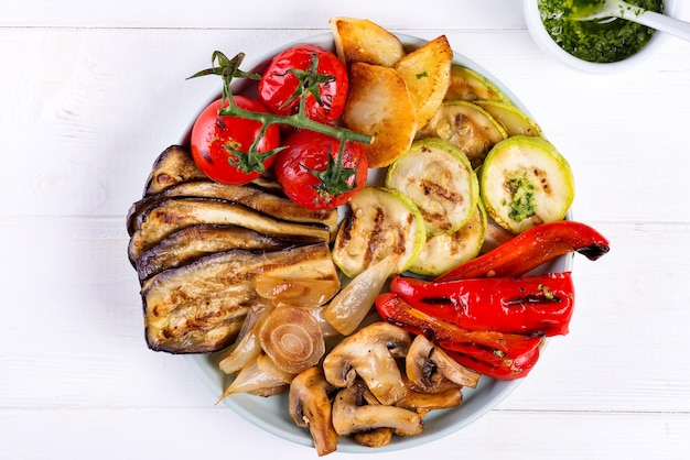 Grilled vegetables on a plate with pesto on white wood