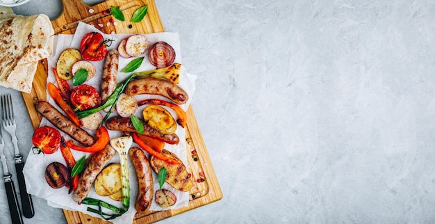 Grilled vegetables and sausages on wooden board top view