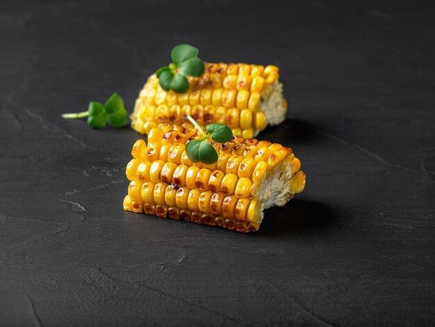 Grilled yellow corn on the cob with green sprouts on a black background Closeup shot Side view Copy space