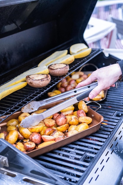 Grilling small potatoes with slices of garlic on an outdoor gas grill.