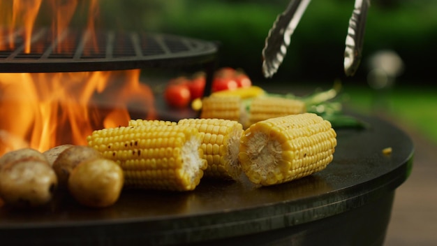 Grilling vegetables cooking on fire outside Man hands turning corn with forceps