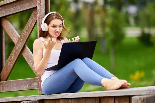 Grimacing woman makes video call using laptop outdoors