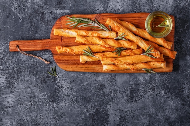 Grissini bread sticks on wooden cutting board  over concrete textured surface.